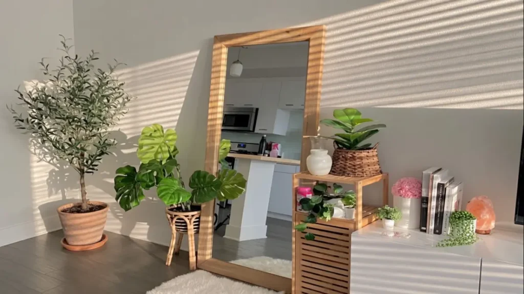 Espelho de corpo inteiro com moldura de madeira clara em um ambiente iluminado por luz natural, rodeado de plantas verdes e móveis de madeira em estilo moderno e aconchegante.