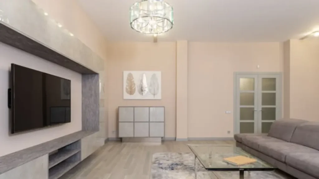 Sala de estar moderna com TV em painel de mármore cinza, sofá cinza, mesa de centro de vidro e lustre de cristal.