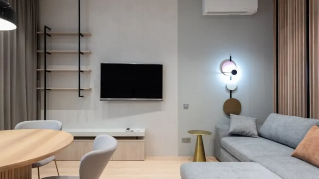 Sala de estar moderna com sofá cinza, TV preta na parede com detalhe de duas cores de tinta, prateleiras de madeira e mesa redonda.
