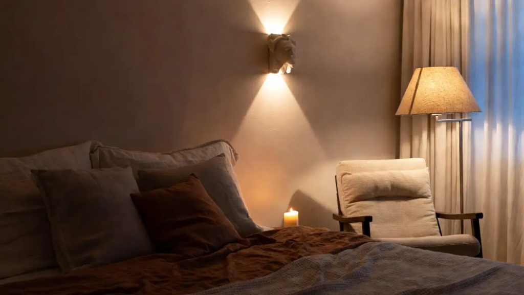 Quarto aconchegante à noite com luz de arandela e abajur de linho, cama com tons terracota.