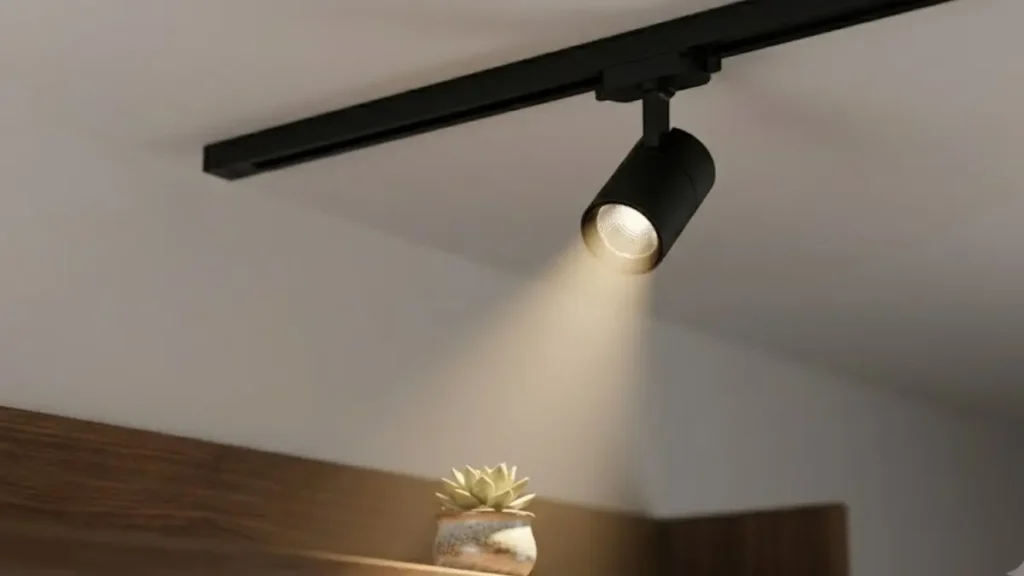 Spot de LED preto em um trilho de teto projetando um cone de luz direcionada sobre um pequeno vaso de planta.