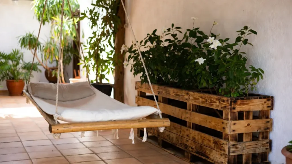 Rede suspensa ao lado de jardineira feita de pallet de madeira com plantas floridas