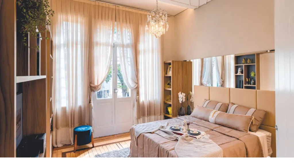 Quarto com janela grande e com cortinas transparente deixa a luz do sul raiar.